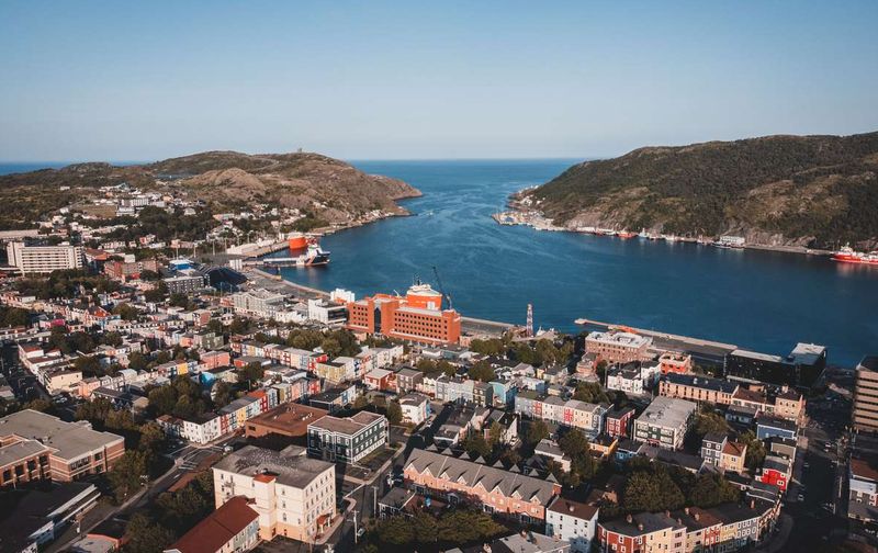 Aerial view of colorful houses and a harbor in St. John's, Newfoundland, surrounded by coastal hills.