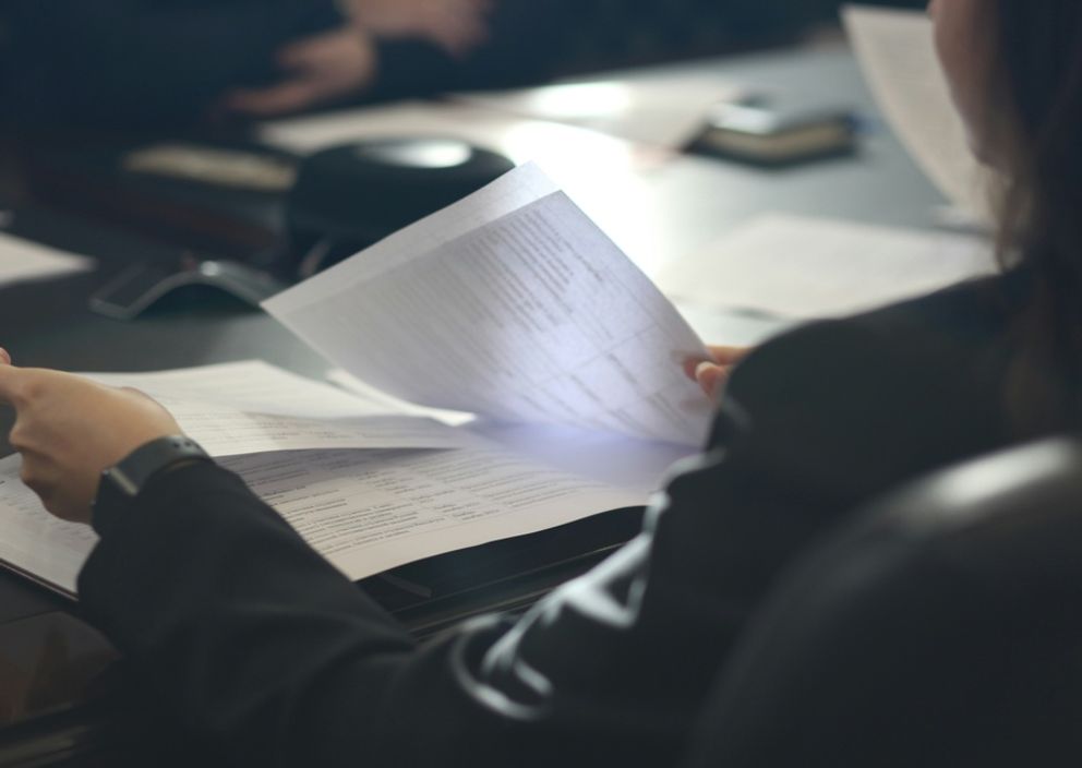 A person in a dark suit reviewing and flipping through printed documents at a meeting table.