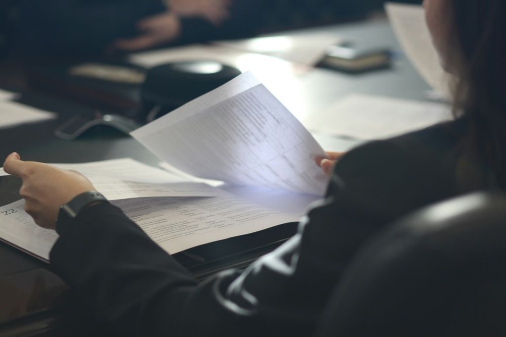 A person in a dark suit reviewing and flipping through printed documents at a meeting table.