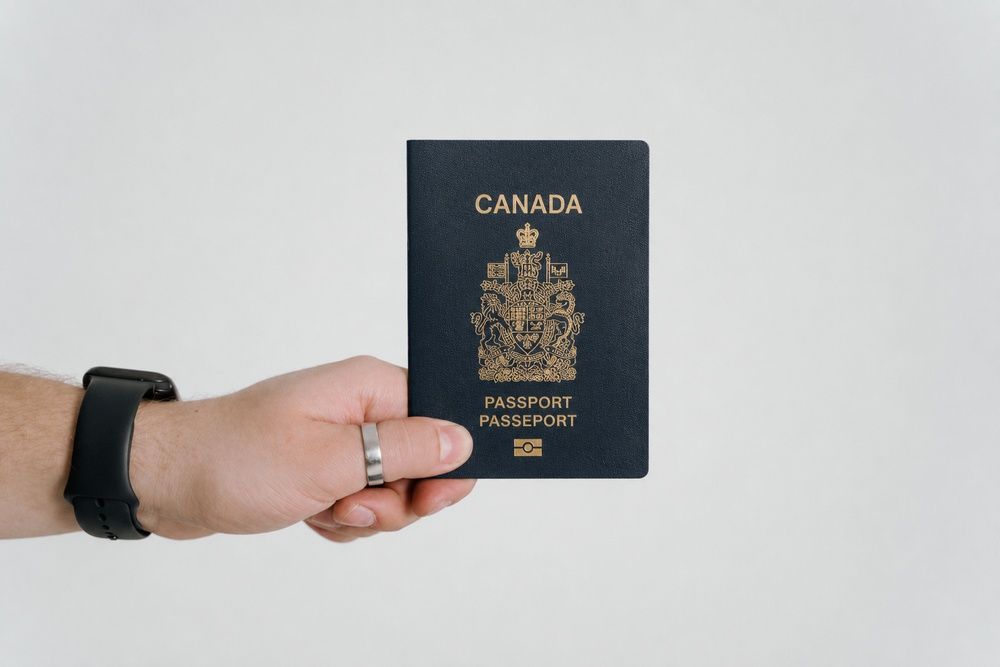 A hand holding a dark blue Canadian passport against a plain light background.
