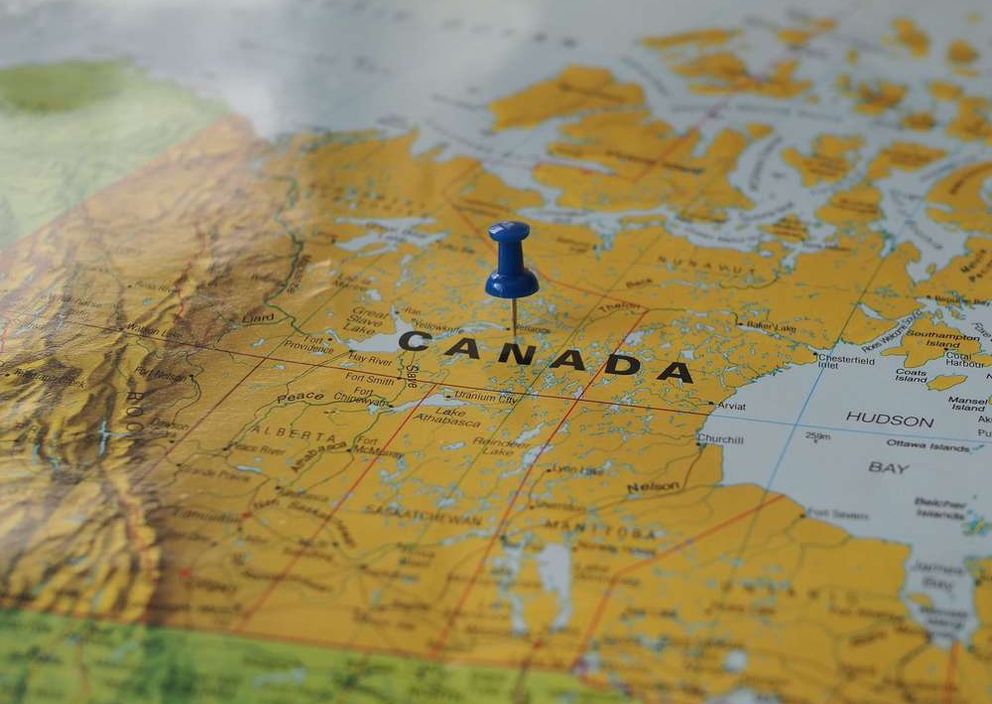 Close-up of a blue pushpin pinned on a map of Canada.