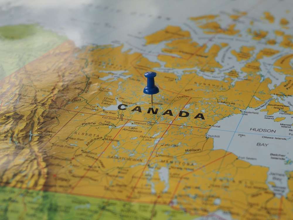 Close-up of a blue pushpin pinned on a map of Canada.