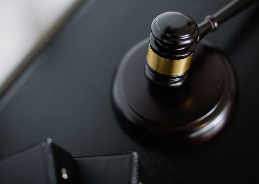 A wooden judge's gavel with a gold band resting on its sound block.