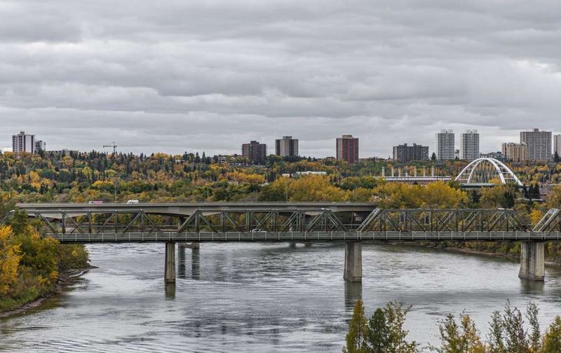 Bridges over the South Saskatchewan River in Saskatoon, showing the city skyline and yellow autumn trees.