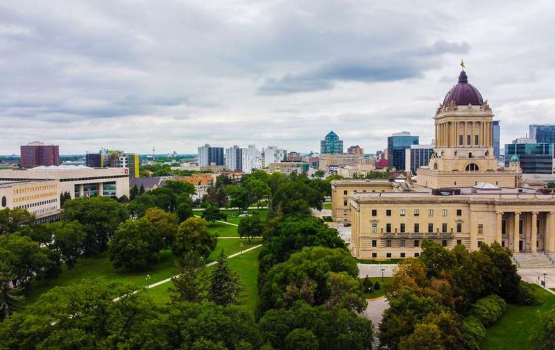 Aerial view of the Manitoba Legislative Building and surrounding park in Winnipeg under a cloudy sky.