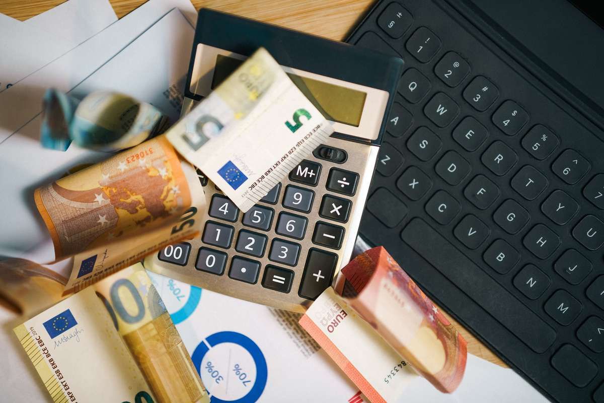 Euro banknotes, a calculator, financial charts, and a laptop keyboard on a desk.