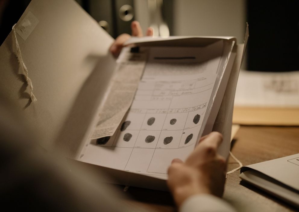 A person holds open a file folder displaying an official document with black ink fingerprints.