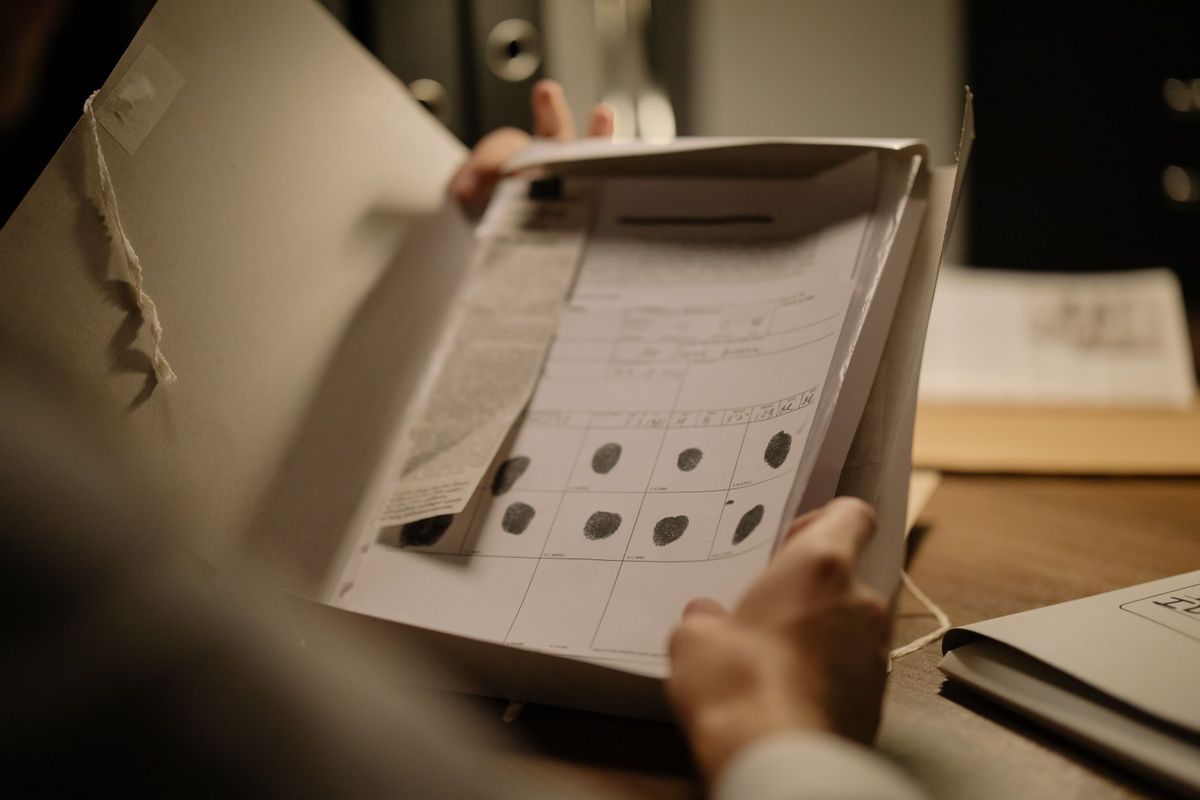 A person holds open a file folder displaying an official document with black ink fingerprints.