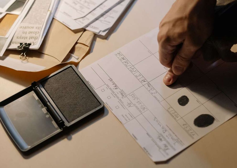 A hand pressing a finger onto an official fingerprint form next to an open ink pad.