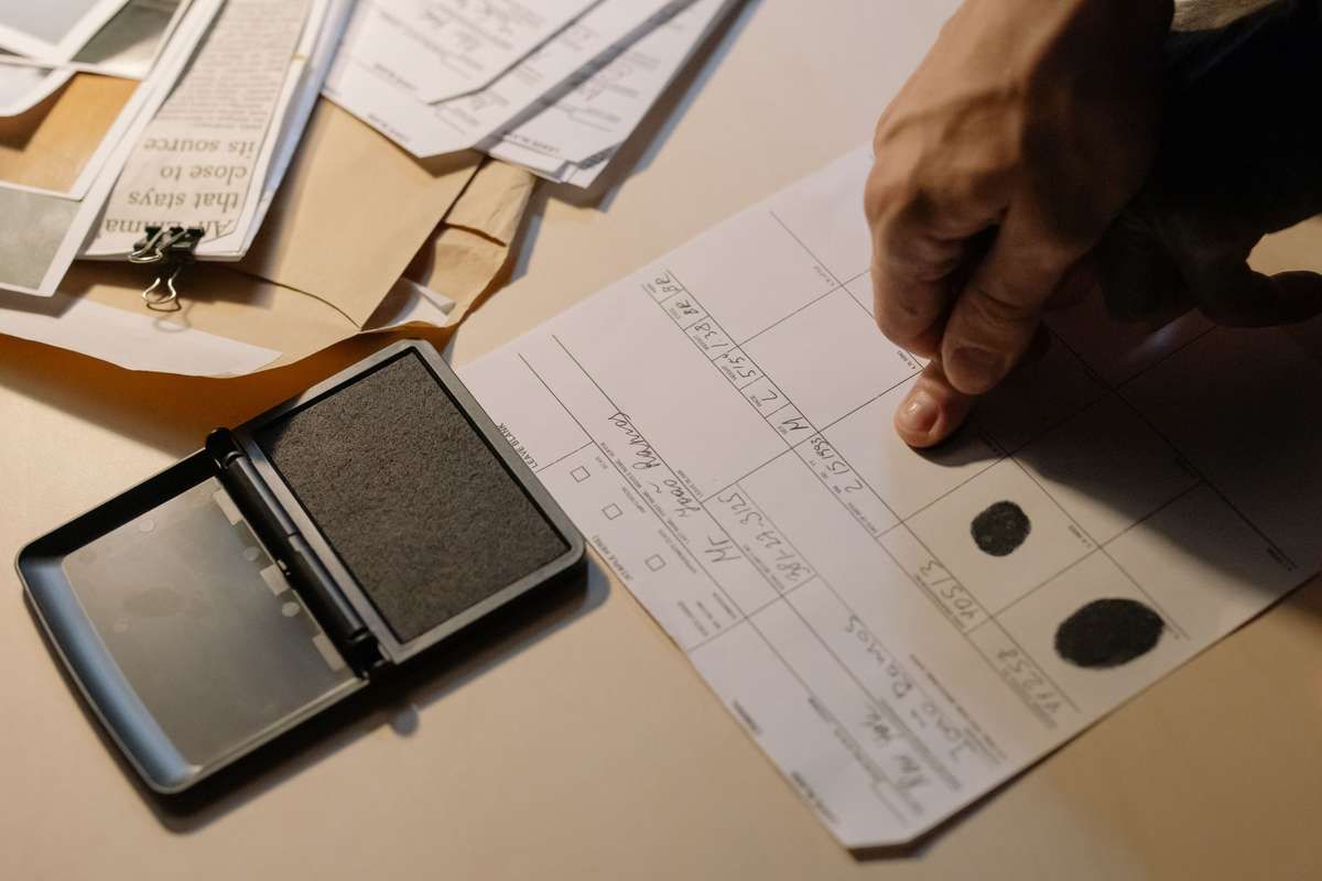 A hand pressing a finger onto an official fingerprint form next to an open ink pad.