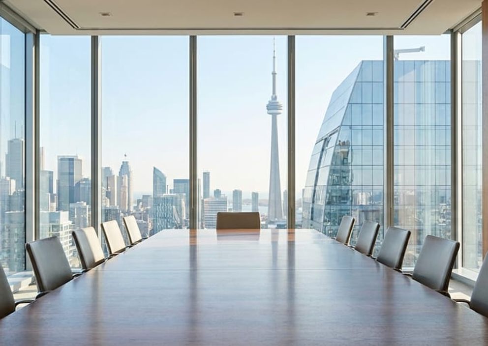 A bright, modern executive boardroom overlooking a clean Canadian city skyline through large glass windows.